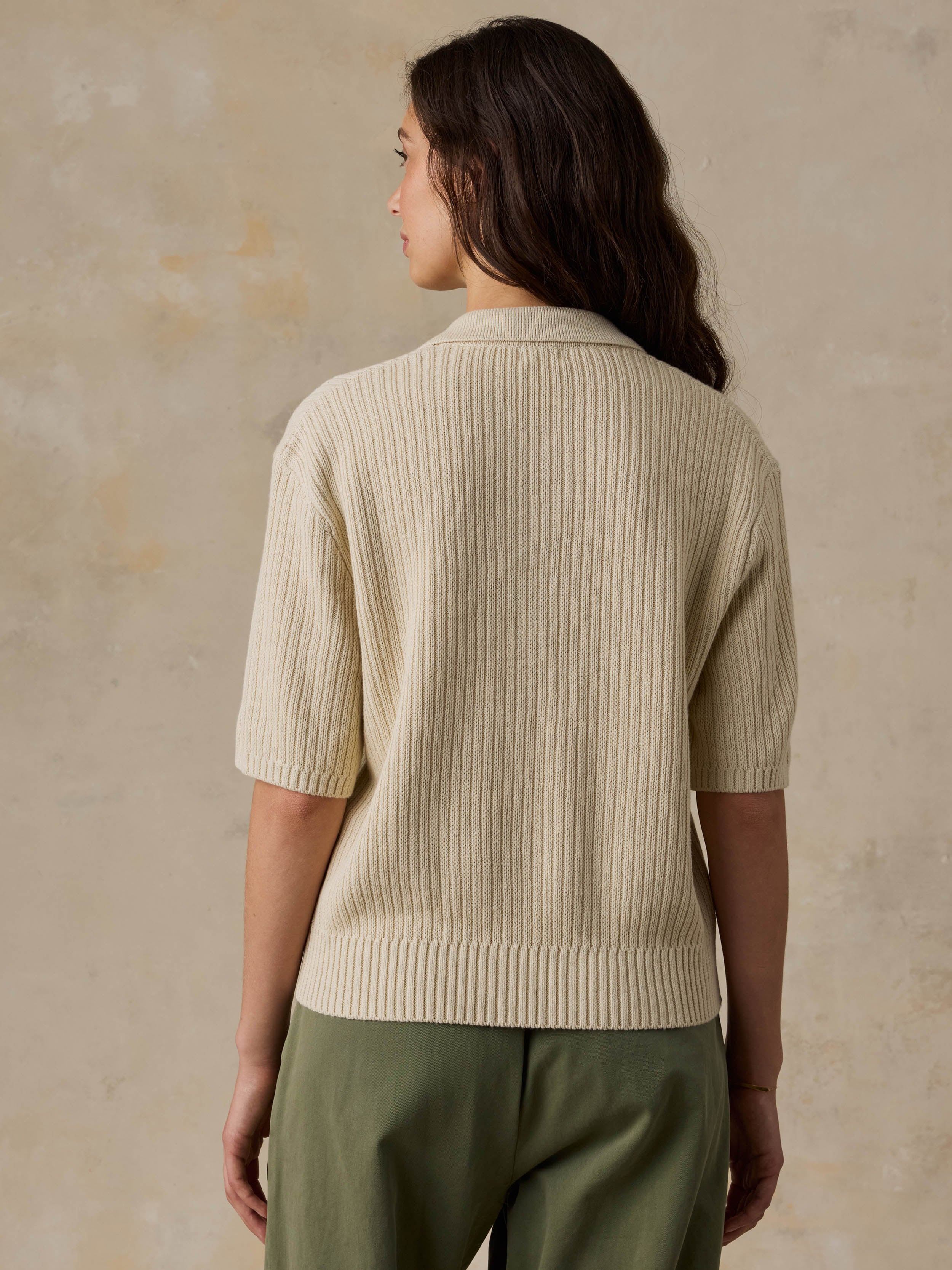 Woman wearing a beige polo and green pants against a beige background