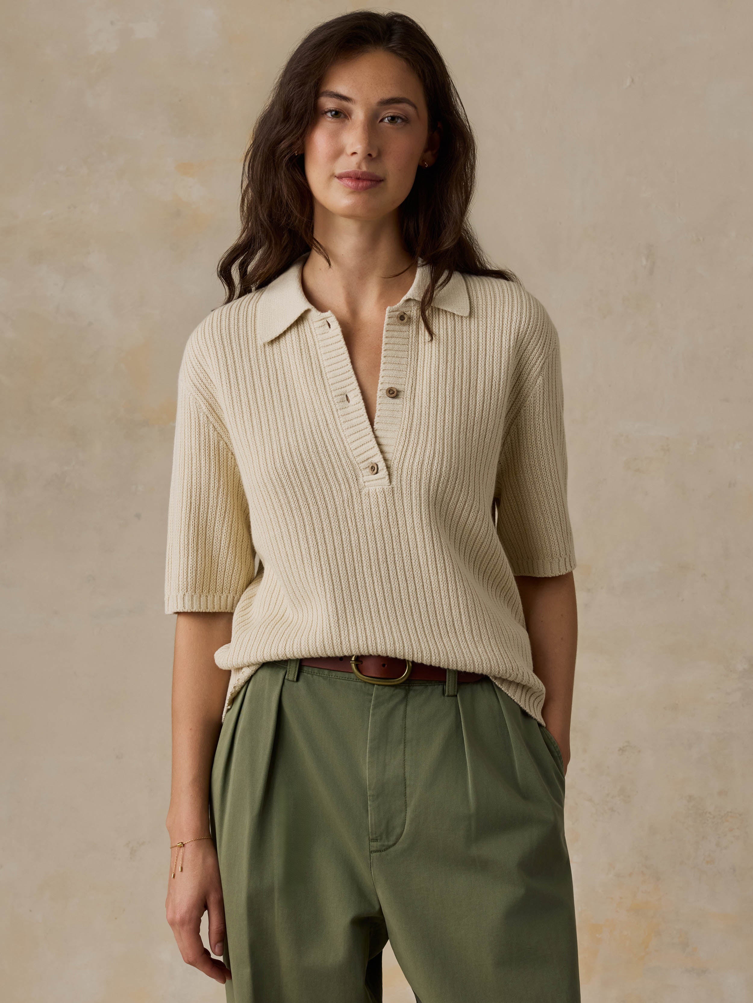 Woman wearing a beige polo and green pants against a beige background
