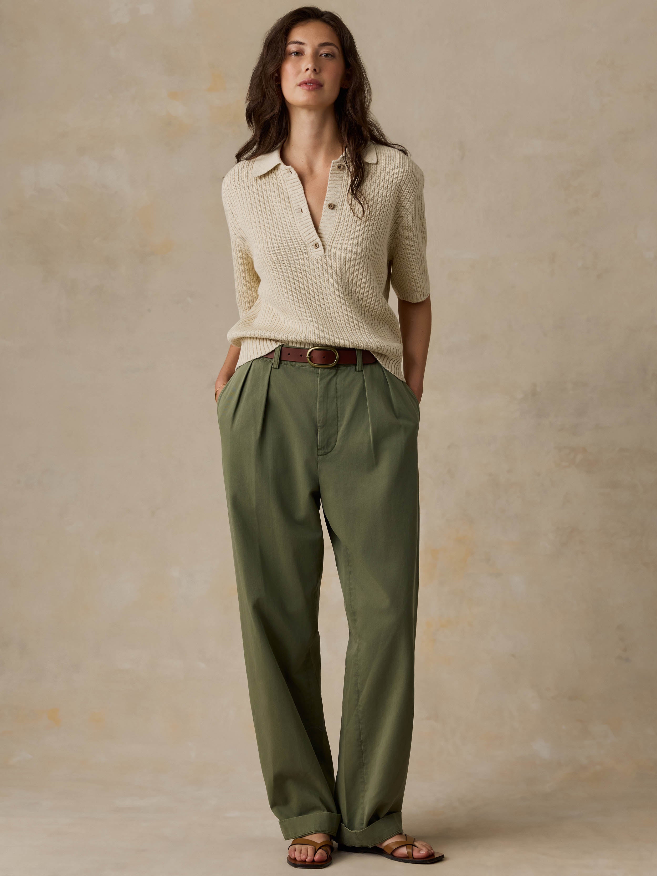 Woman wearing a beige polo and green pants against a beige background