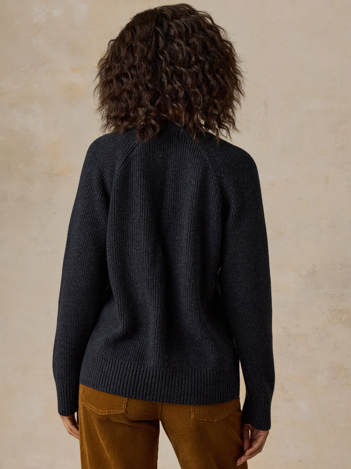 A woman wearing a dark charcoal ribbed knit sweater and brown corduroy pants, image 2 of 6