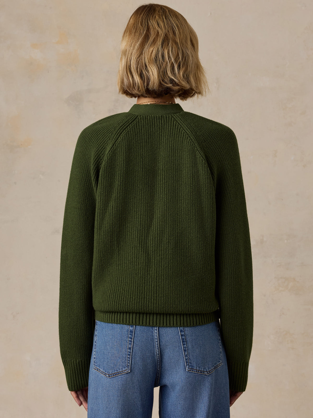 A woman wearing an olive green ribbed knit sweater and blue jeans, image 3 of 6