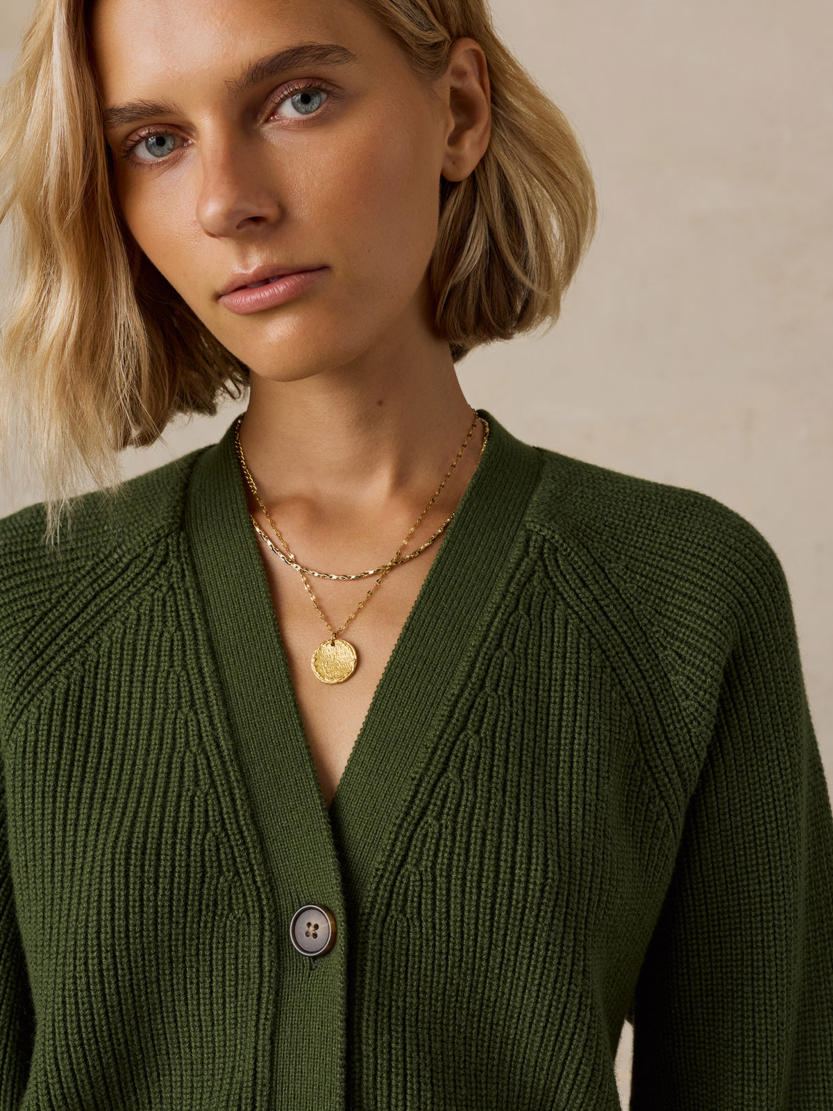 A close-up of a woman wearing an olive green ribbed cardigan sweater, image 2 of 6