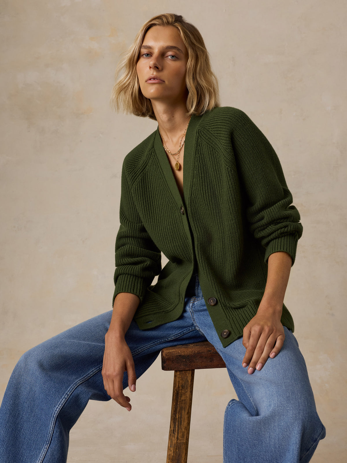 A woman wearing an olive green ribbed knit cardigan, blue wide-leg jeans, image 5 of 6