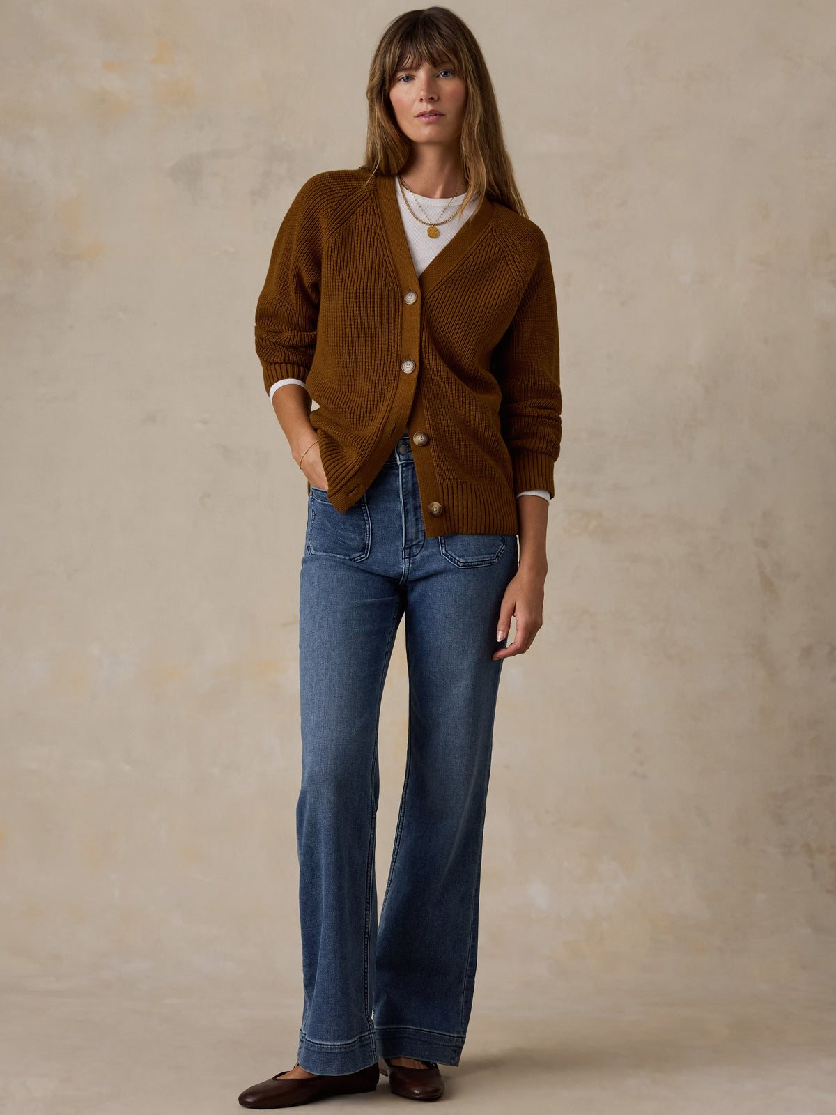 A woman wearing a brown ribbed cardigan over a cream top, blue flare jeans, and dark brown flats., image 5 of 5