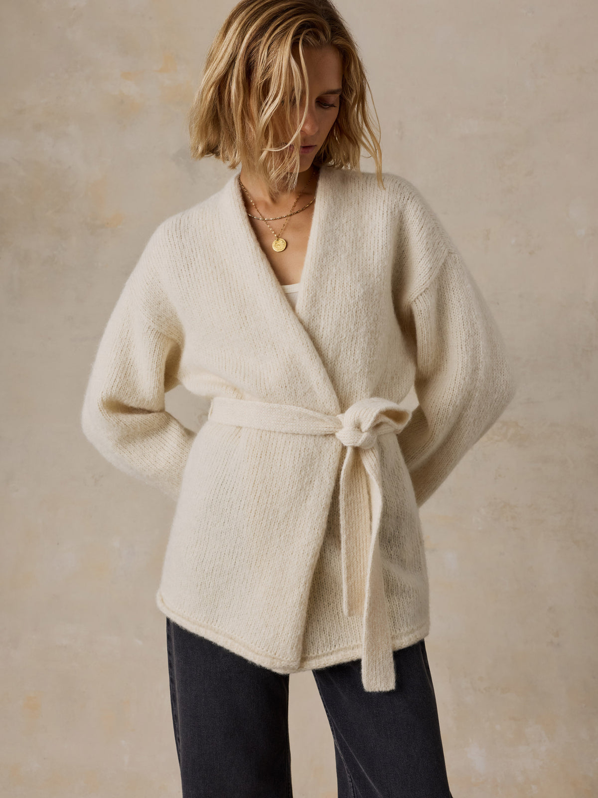 A woman wearing a cream wrap cardigan and black jeans, image 6 of 8