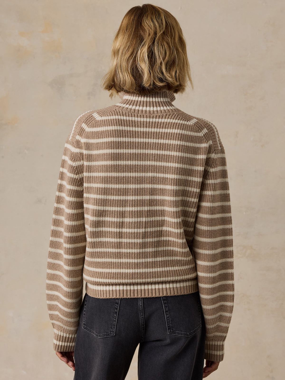 A woman wearing a beige and brown striped quarter-zip pullover sweater with dark wash jeans, image 4 of 5