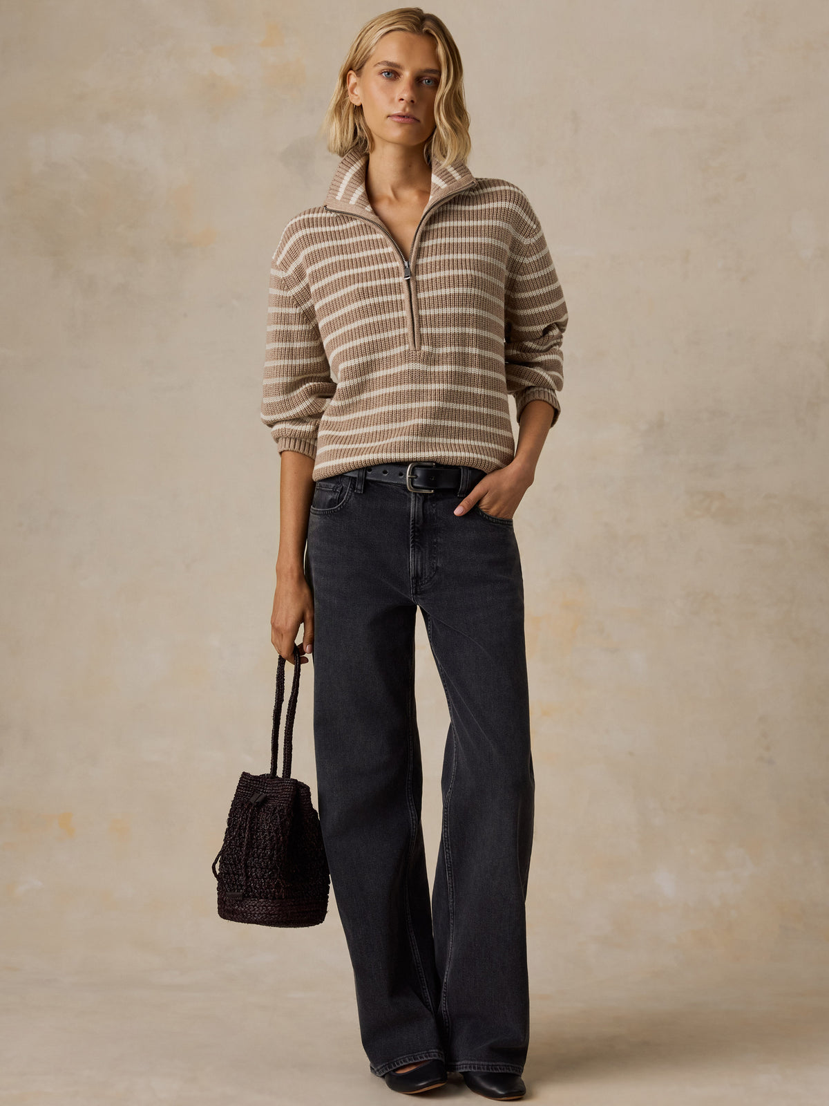 A woman wearing a beige and brown striped quarter-zip pullover sweater with dark wash jeans and a dark bag, image 2 of 5