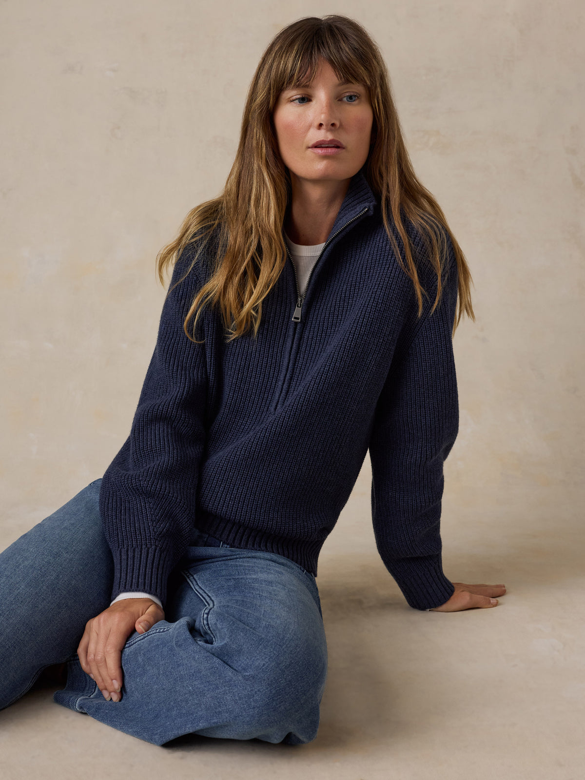 Woman wearing a navy blue quarter zip sweater and blue jeans, image 5 of 6