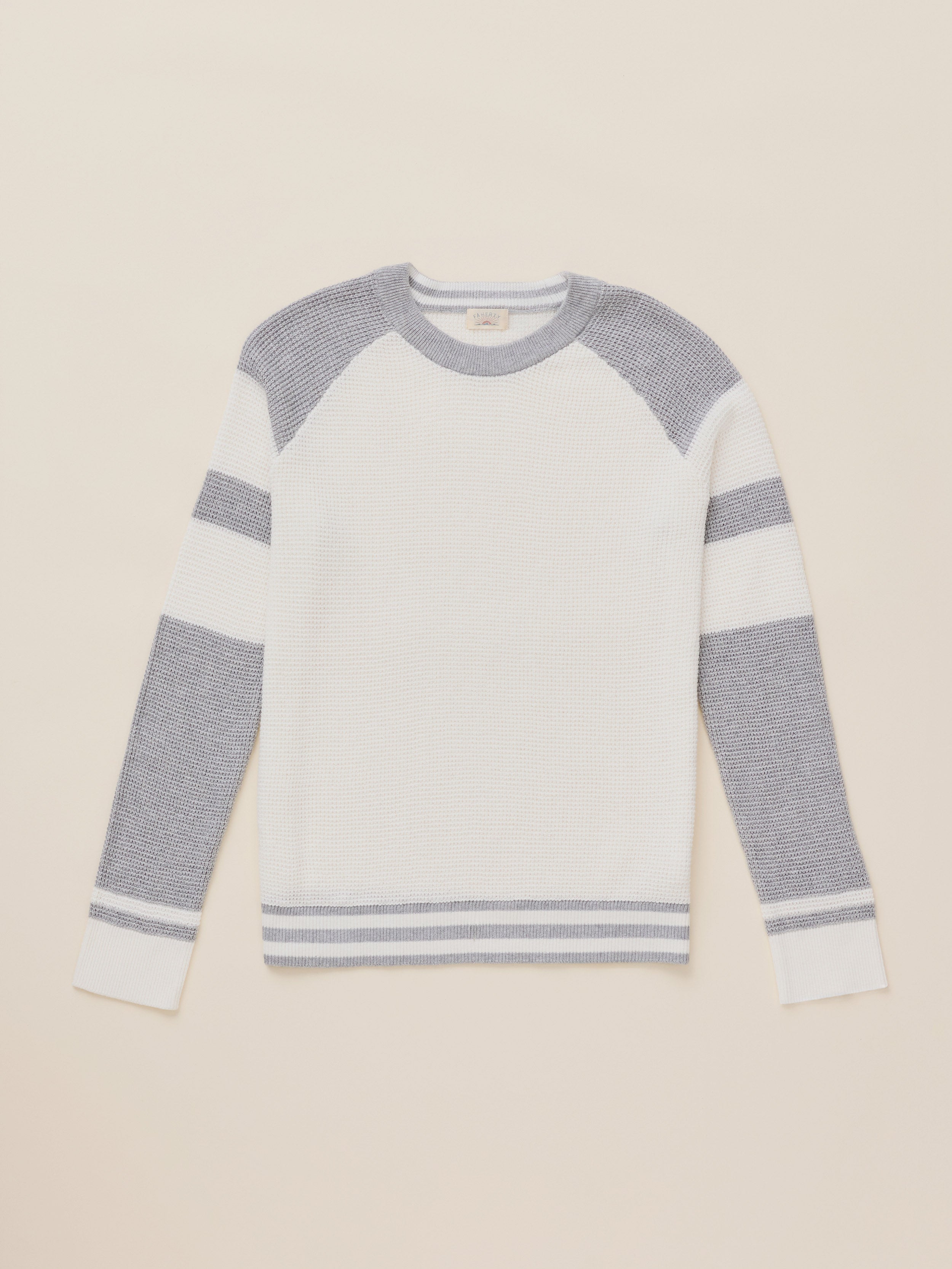 A long-sleeve knit sweater with a white body, gray shoulder yoke, and gray horizontal stripes on the sleeves and hem, displayed flat against a light beige background.