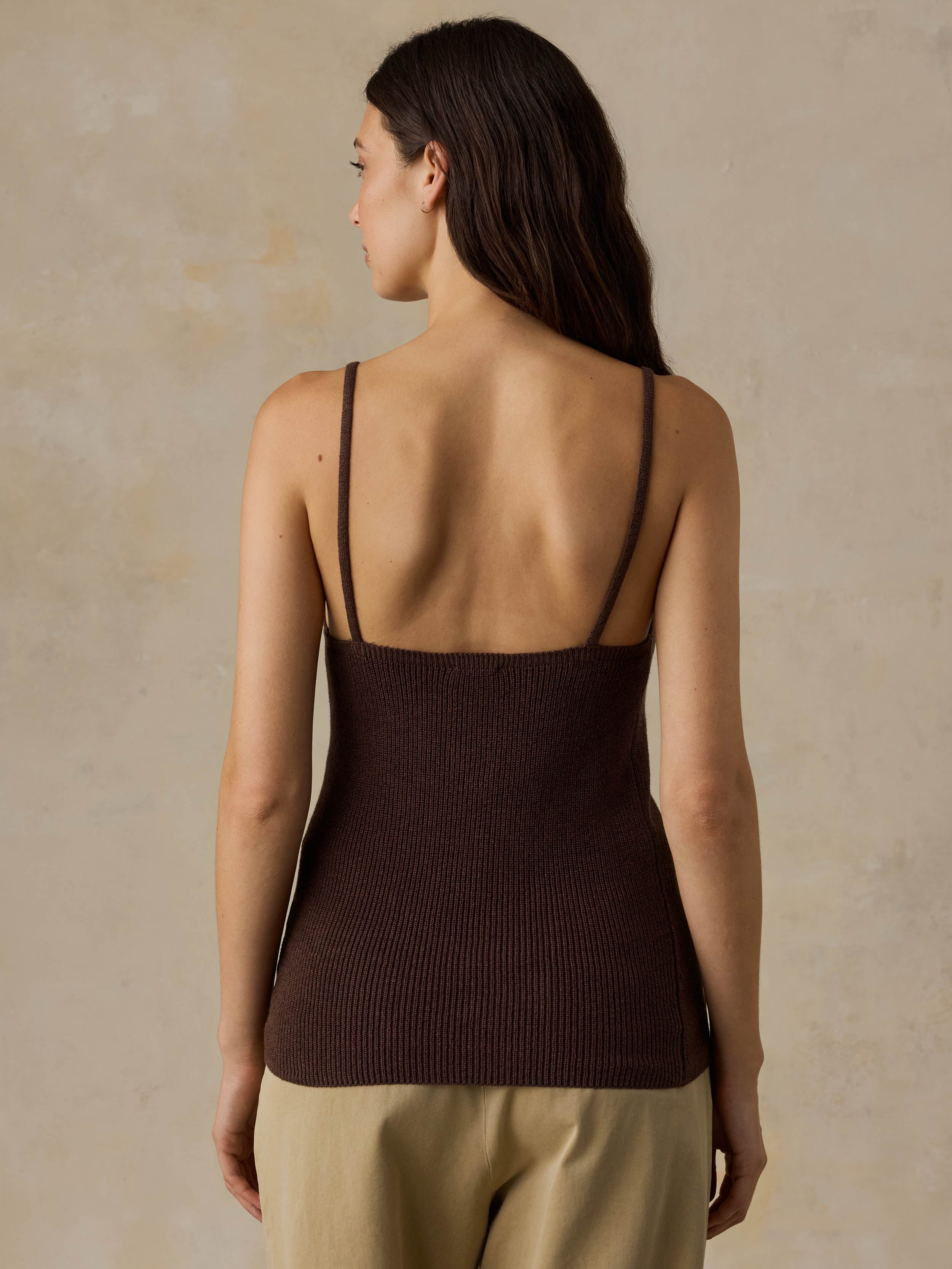 Woman wearing a brown tank top and beige pants against a beige background
