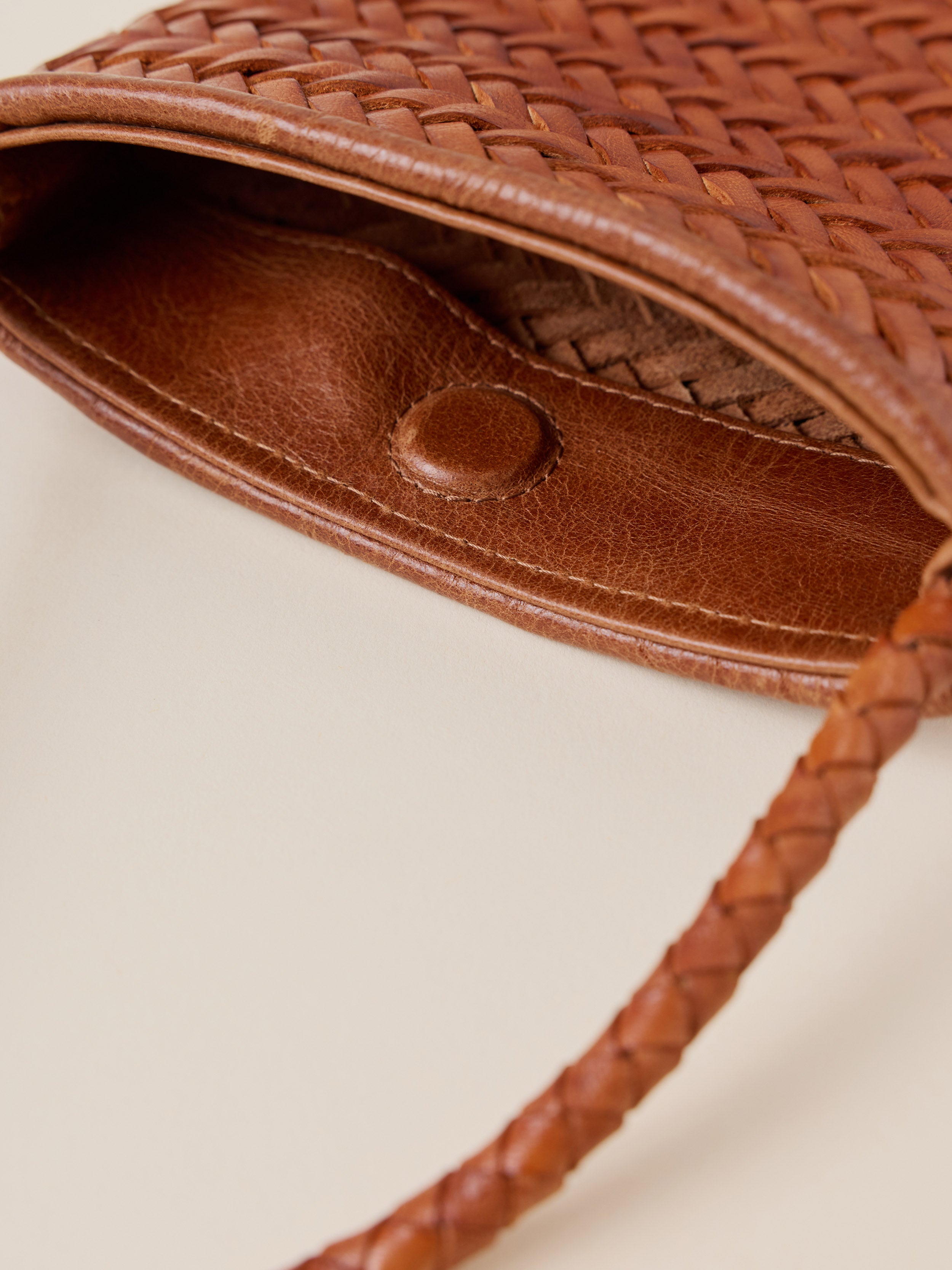 Close-up of a brown woven leather bag showing the interior lining, a snap closure, and part of the braided strap on a light beige background.