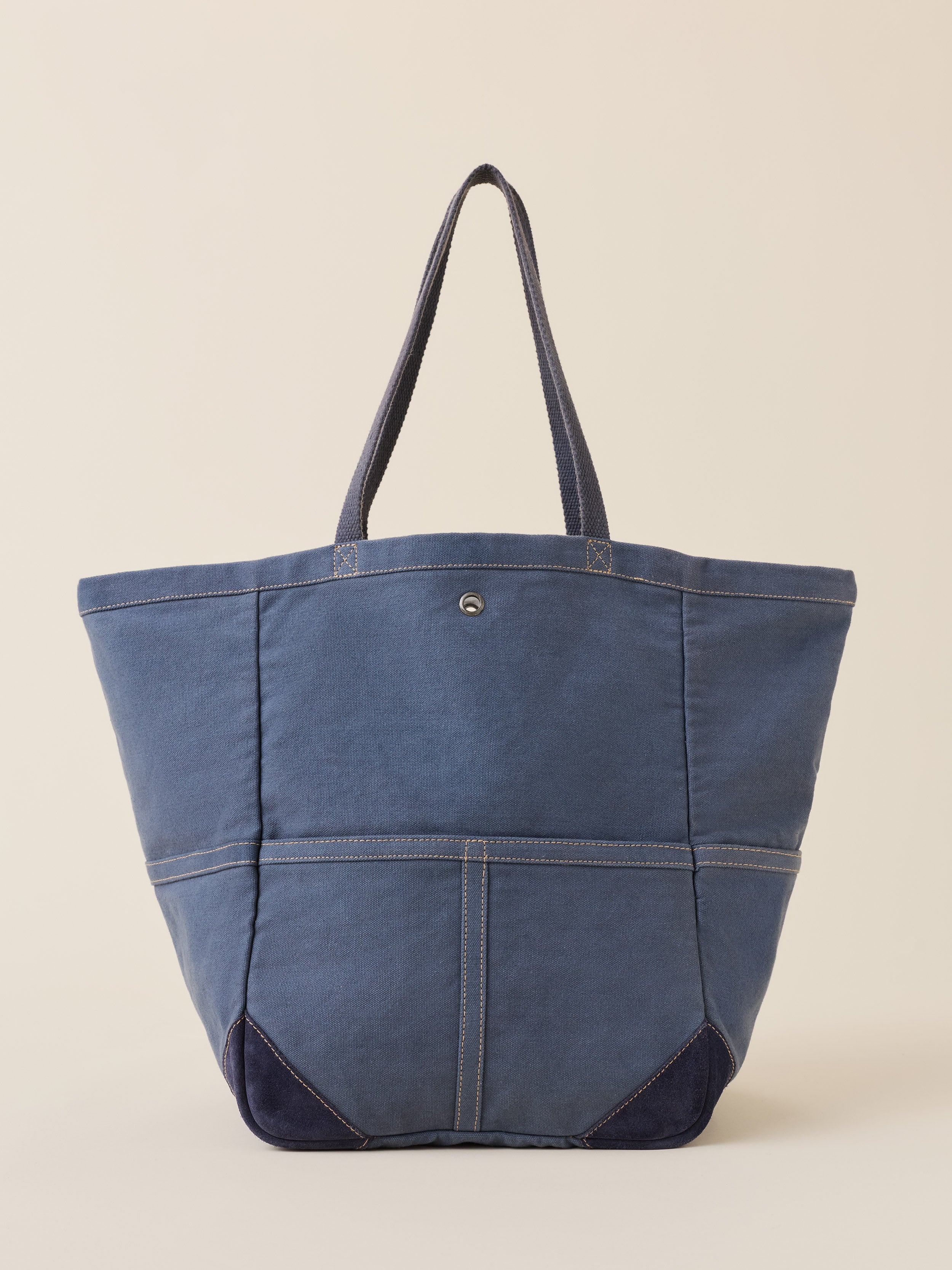 A blue canvas tote bag with dark navy blue contrast panels at the bottom and matching shoulder straps, shown against a solid beige background.