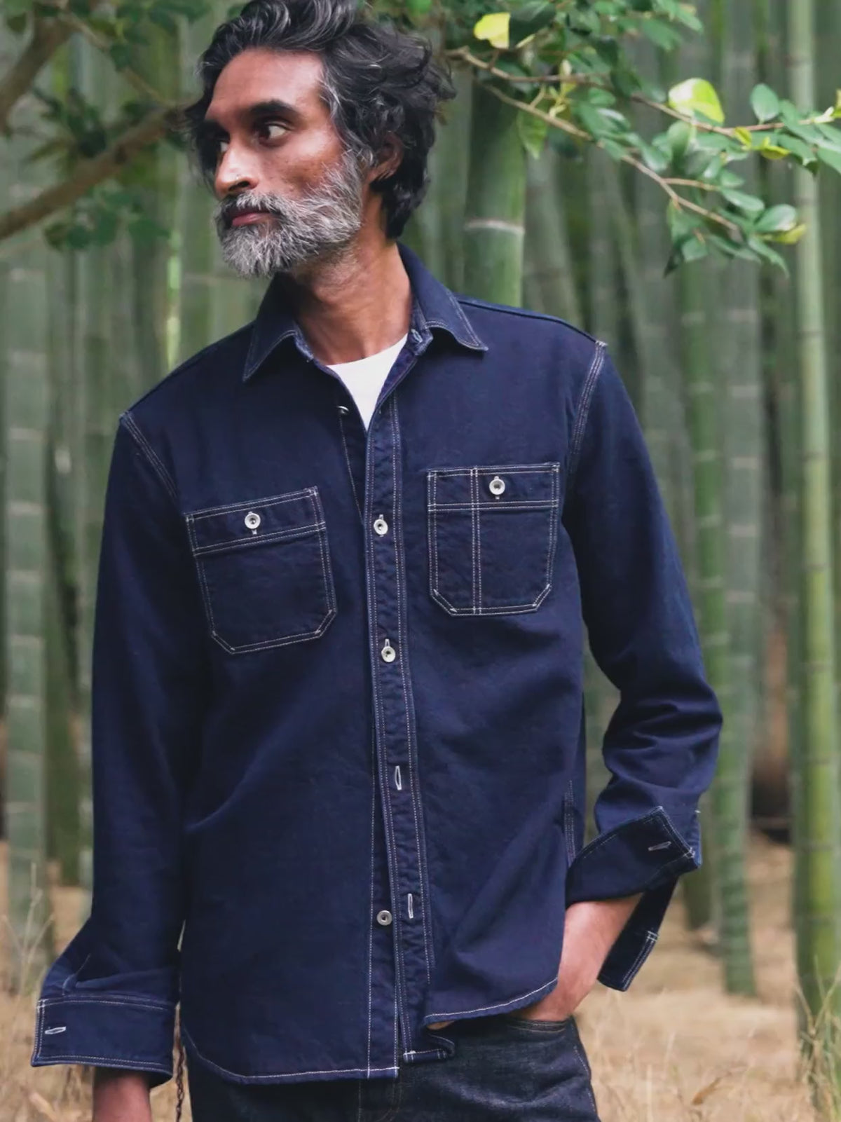 Man wearing an indigo jacket standing outside in a bamboo forest