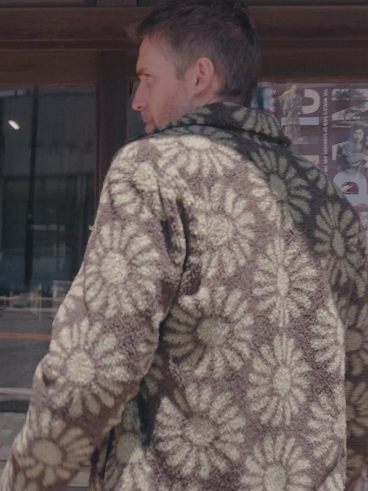 A man wearing a floral printed fleece jacket over a button shirt and blue pants