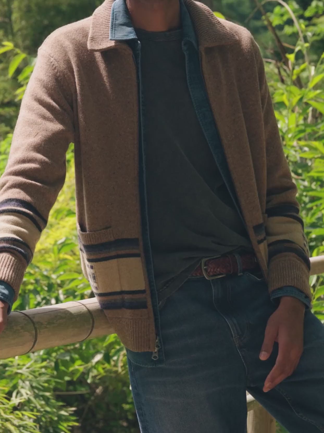 Man wearing a brown zip cardigan over a blue shirt with blue jeans standing outside in nature